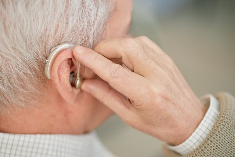 Elderly person adjusting hearing aid behind ear